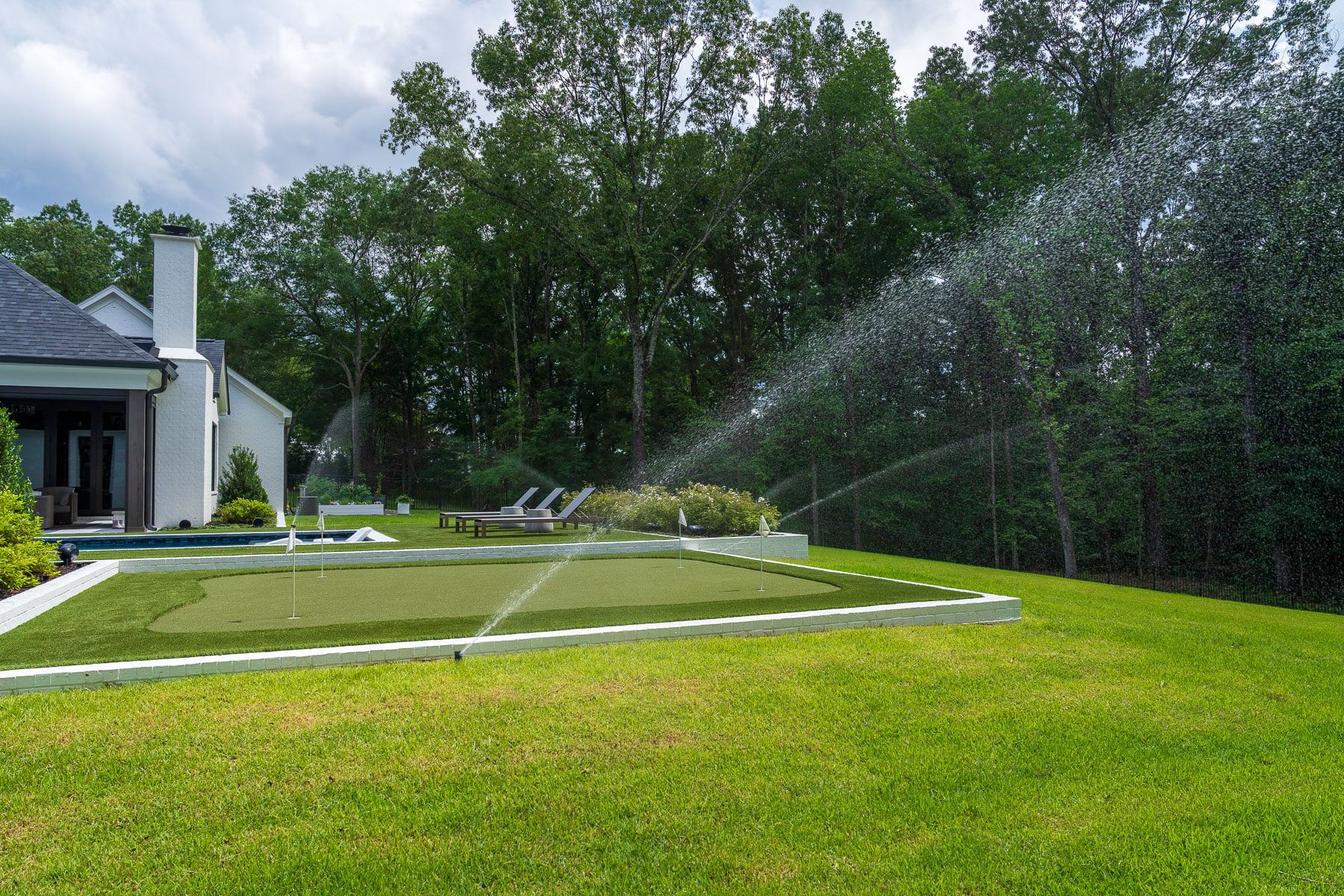 Rotors watering a backyard lawn beside a putting green