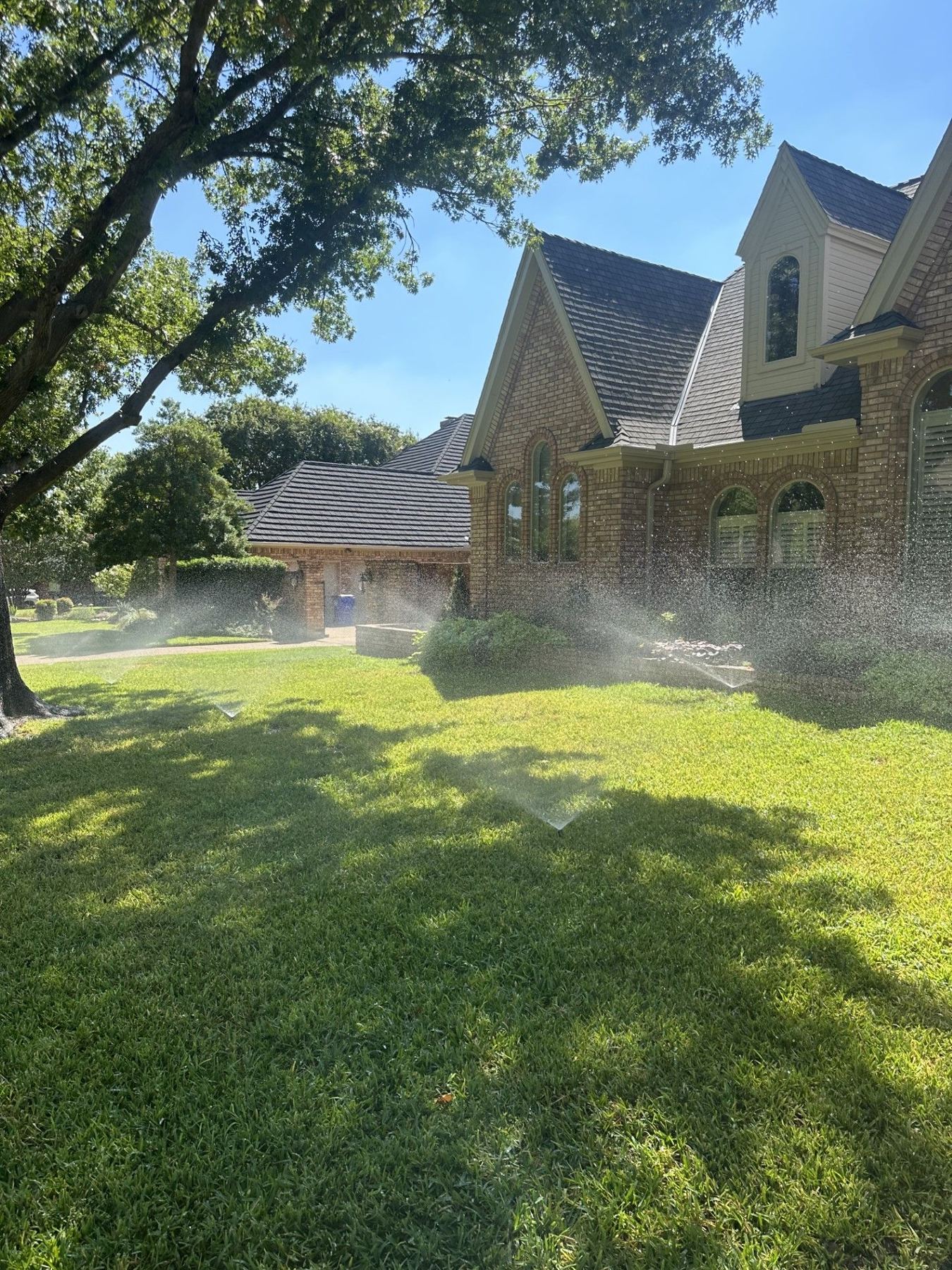 Spray heads watering a St. Augustine lawn in front of a brick home